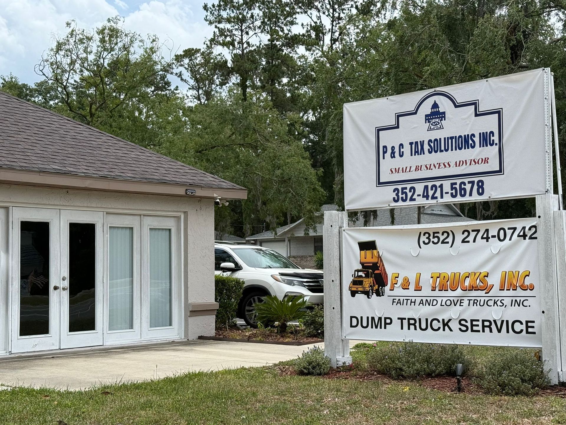 Sign for F&C Tax Solutions Inc. and F&J Trucks Inc. Dump truck service in front of a building; white SUV is visible.