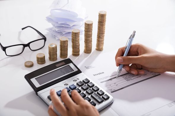 Person calculating with a calculator, writing on paper, and stacks of coins arranged as a rising graph.