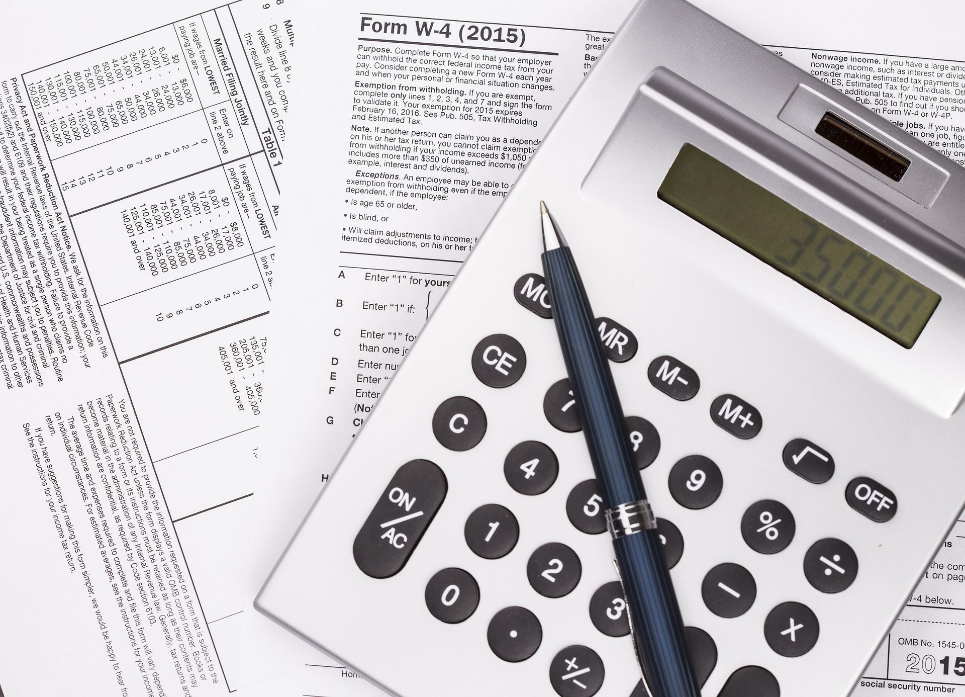 Calculator showing $35,000, pen, and tax forms, suggesting financial calculations or tax preparation on a desk.