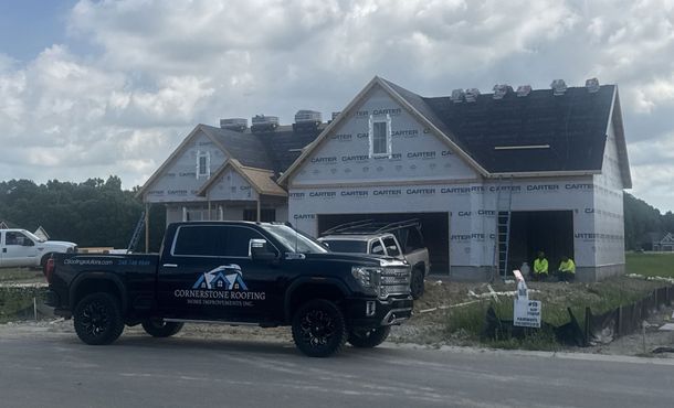 Black truck with company logo parked in front of a house under construction, workers visible.