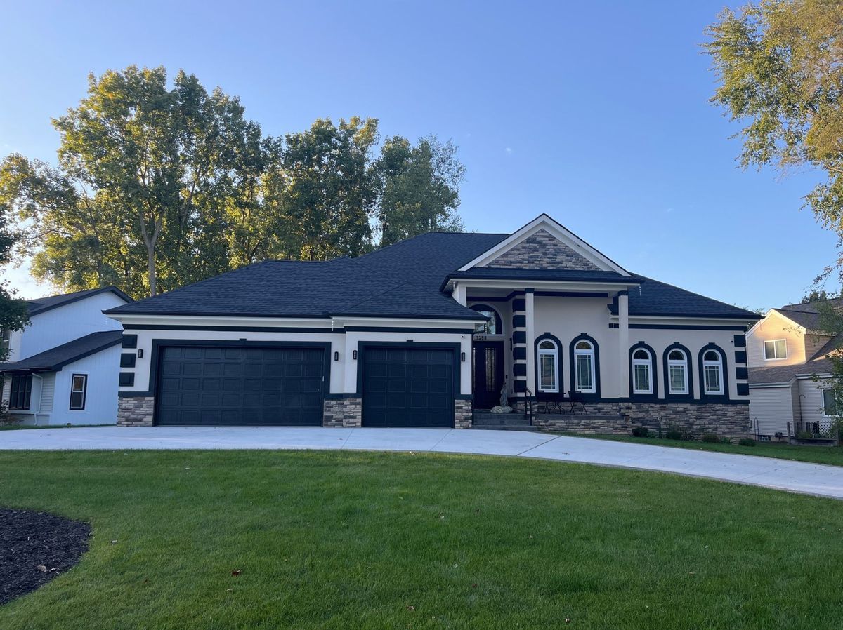 A modern, two-story house with a black roof, two-car garage, and a well-manicured lawn on a sunny day.