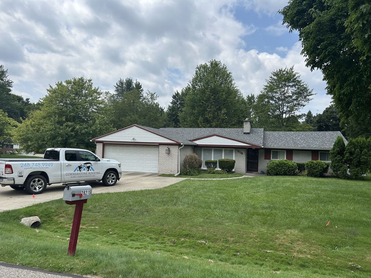 A white truck parked in front of a one-story house with a garage. Green grass and trees surround the house.