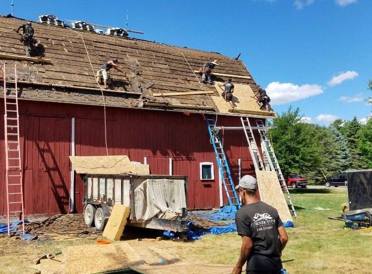Roofers replacing shingles on a red barn under a blue sky.