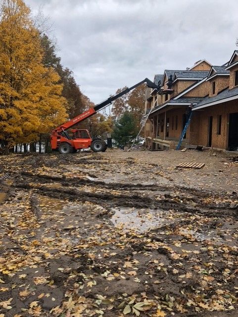 Construction site with a telescopic forklift and building under construction in a muddy lot. Autumn leaves.