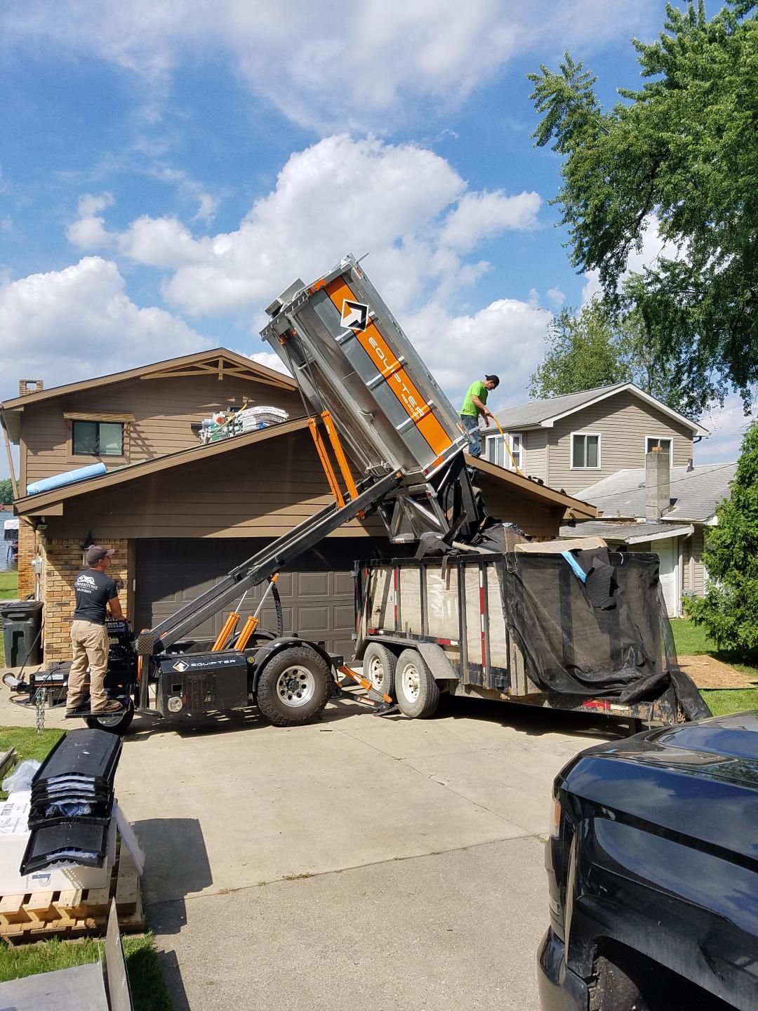 Workers removing a roof; a truck lifts debris from the house. Sunny day.