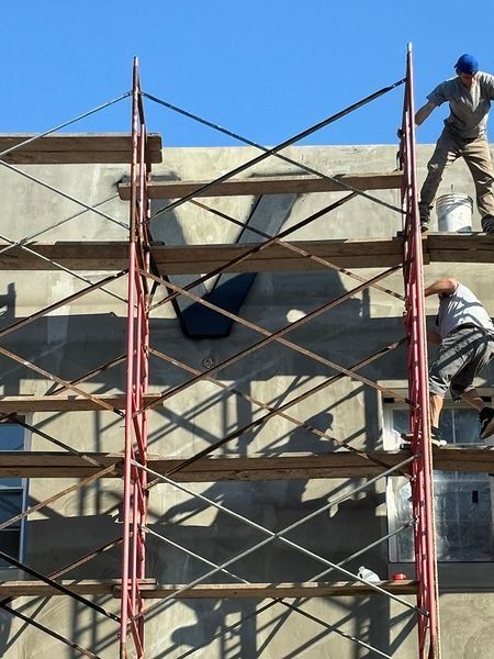 Construction workers on scaffolding repair a building's exterior, set against a blue sky.