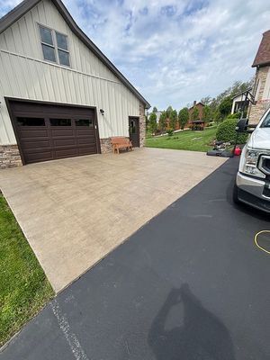 A brown garage and paved area next to a black driveway and green lawn on a cloudy day.