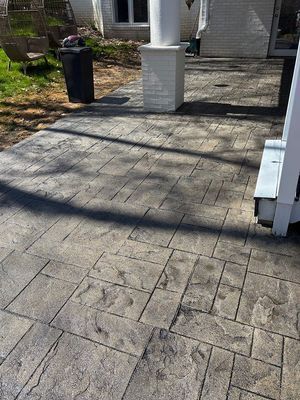 Stamped concrete patio with gray flagstone pattern, next to a white column and building.