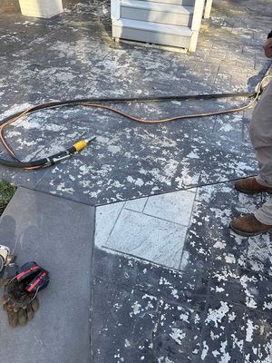 Person working on damaged concrete patio with tool and hose. Gloves are on the ground.