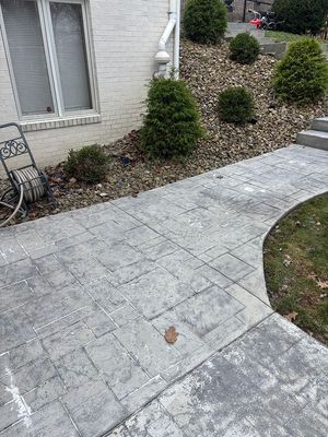 Gray stamped concrete walkway next to a house with a garden of shrubs and gravel.
