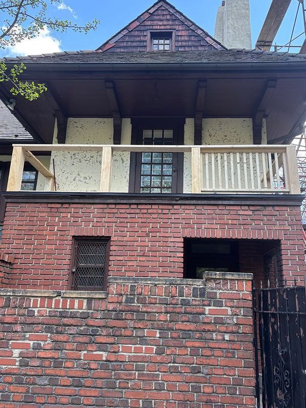 Two-story brick building with brown accents, upper balcony, and dark roof. Under construction, new wooden rails.