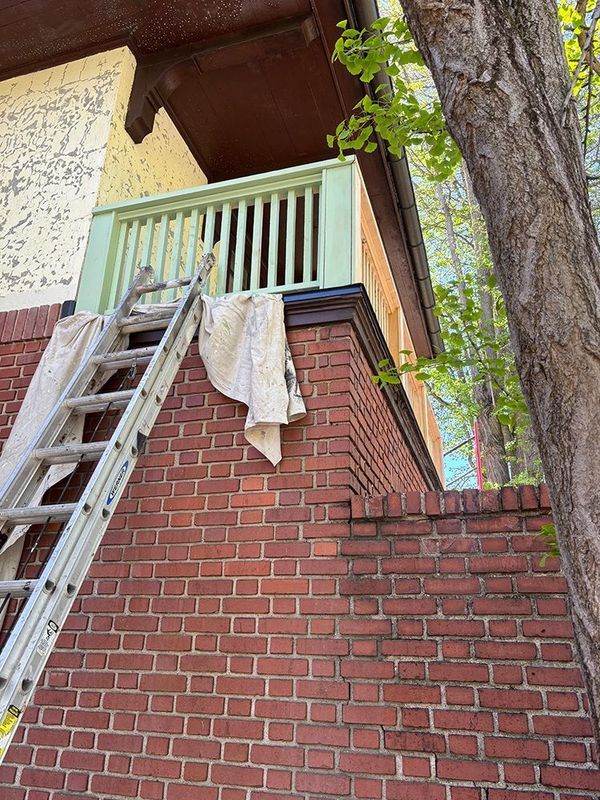 Ladder leaning against brick wall, green-railed porch under a brown roof, a canvas covering.