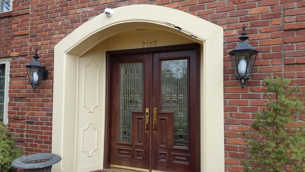 Brick house entrance with brown double doors, tan trim, and black lanterns.