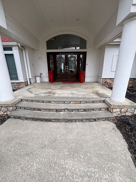 Concrete steps leading to a building entrance with red door and pillars.