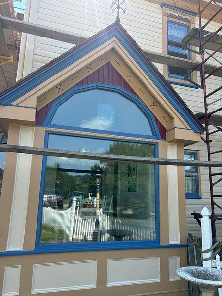 Large window on a house with decorative trim, scaffolding, and a clear reflection of the outside world.