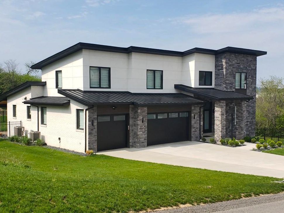 Modern two-story house with white siding, black trim, and gray stone accents. Two-car garage.