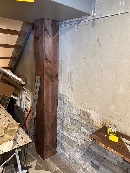 Brown support post next to a stone-tiled wall and stairs in a basement under renovation.