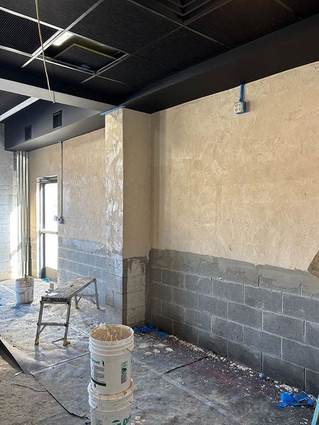 Construction site interior: cement block wall, plaster, black ceiling, doorway, paint buckets, tools.