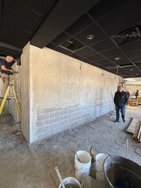 Construction site: two men working on a wall. Cement blocks, gray plaster, black ceiling.