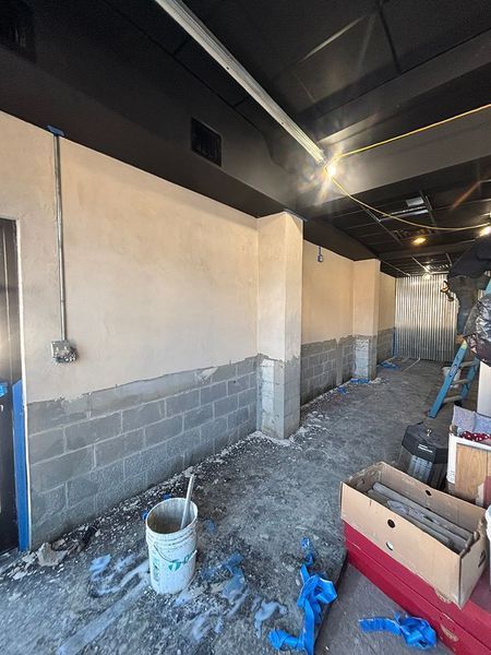 Interior construction: concrete block walls with plaster, dark ceiling, and tools.