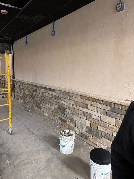 Interior wall with stone wainscoting and plastered upper section, construction site with a ladder and buckets.