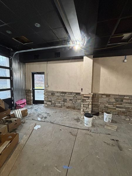 Interior construction site; stone wall, black ceiling, metal door, materials, concrete floor.