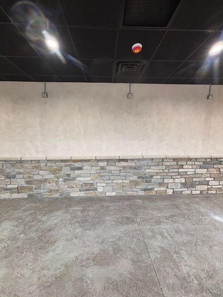 Empty room with gray stone wall, plastered wall, and concrete floor. Overhead lighting.