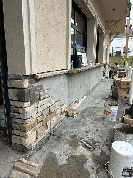 Stone veneer being installed on the exterior wall of a building; person working.