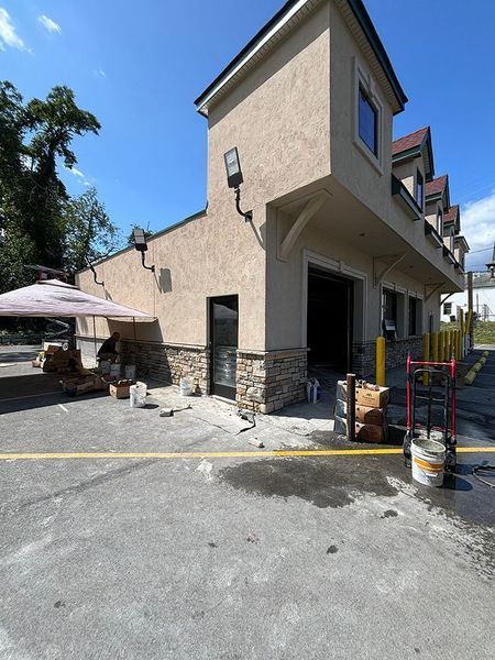 Exterior of a beige building with a garage door and a small umbrella-covered seating area; construction materials present.