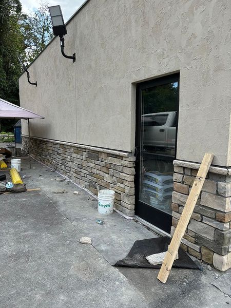 Exterior of a building with stone veneer, a black door, and work in progress.