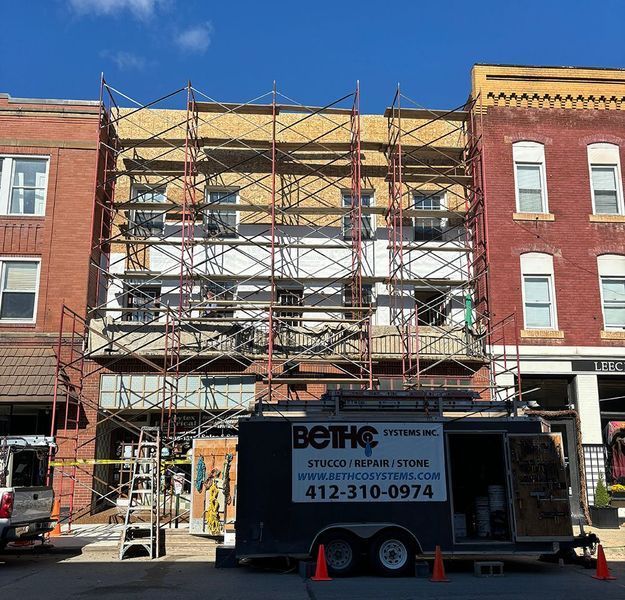 Building facade with scaffolding during renovation; yellow brick, red brick, and a black trailer in front.