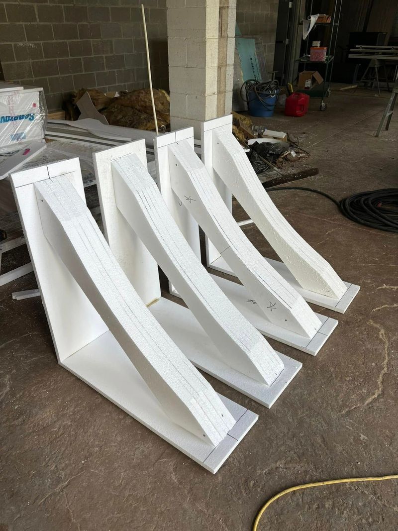 Four white, decorative brackets with curved support beams rest on a brown floor.