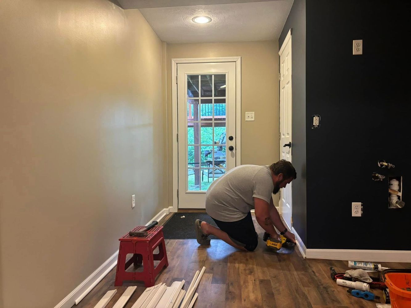 Man installing trim on a floor, a red stool and door in the background.
