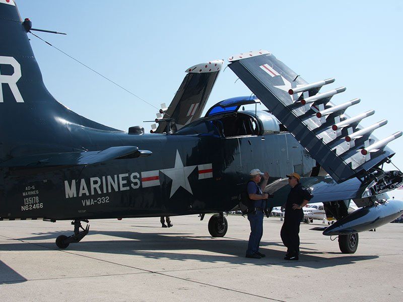 Two men stand in front of a marines plane