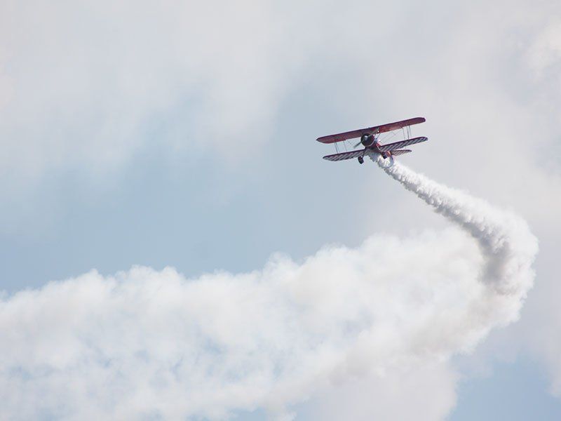 A biplane is flying in the sky with smoke coming out of it.