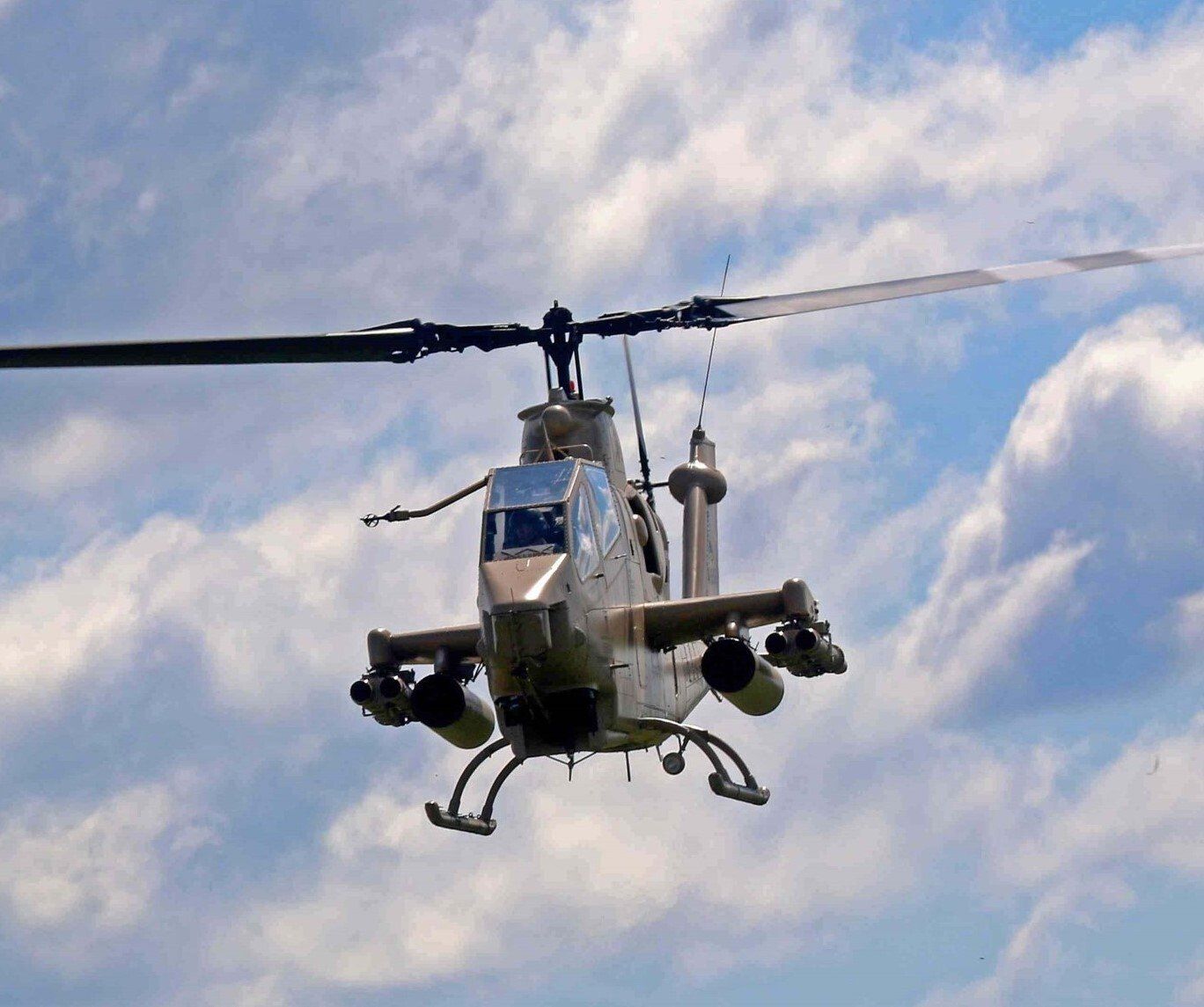 A military helicopter is flying through a cloudy blue sky.