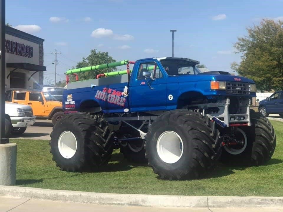 A blue monster truck is parked in a grassy area