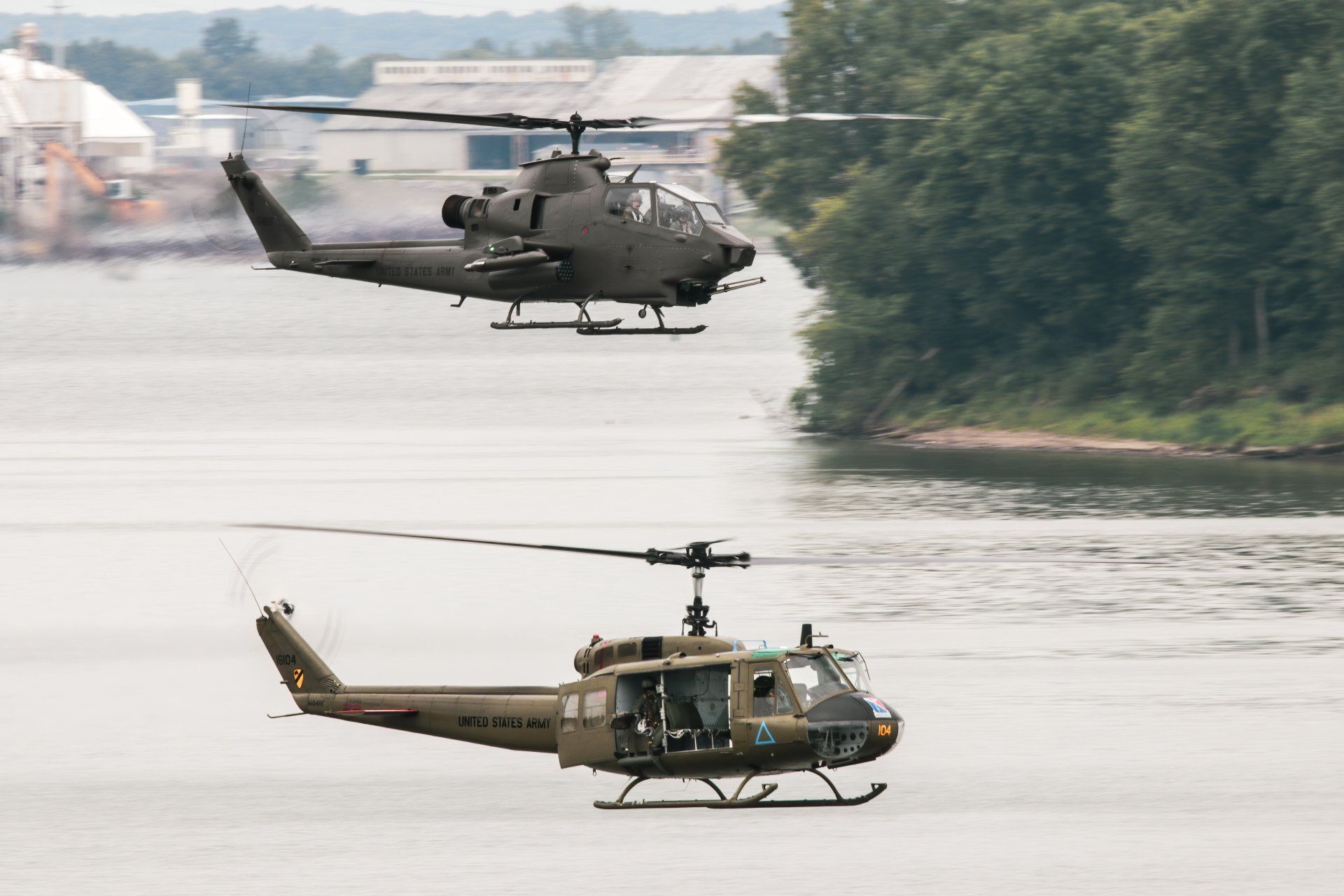 Two military helicopters are flying over a body of water