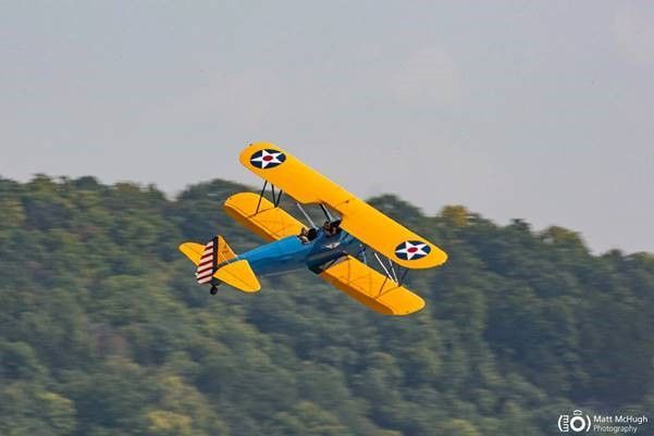 A yellow and blue airplane is flying in the sky over a forest