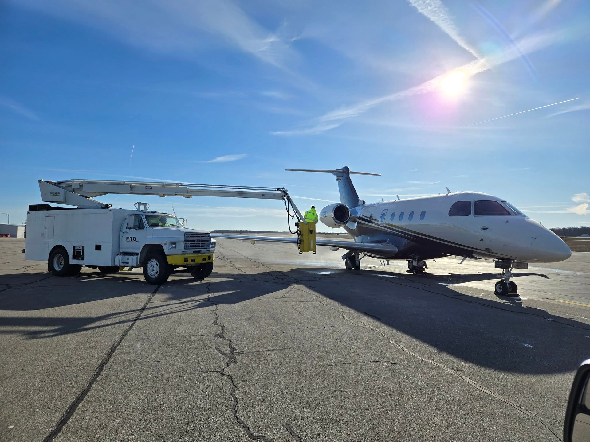 White truck with aerial lift servicing a private jet on a tarmac under a sunny blue sky.