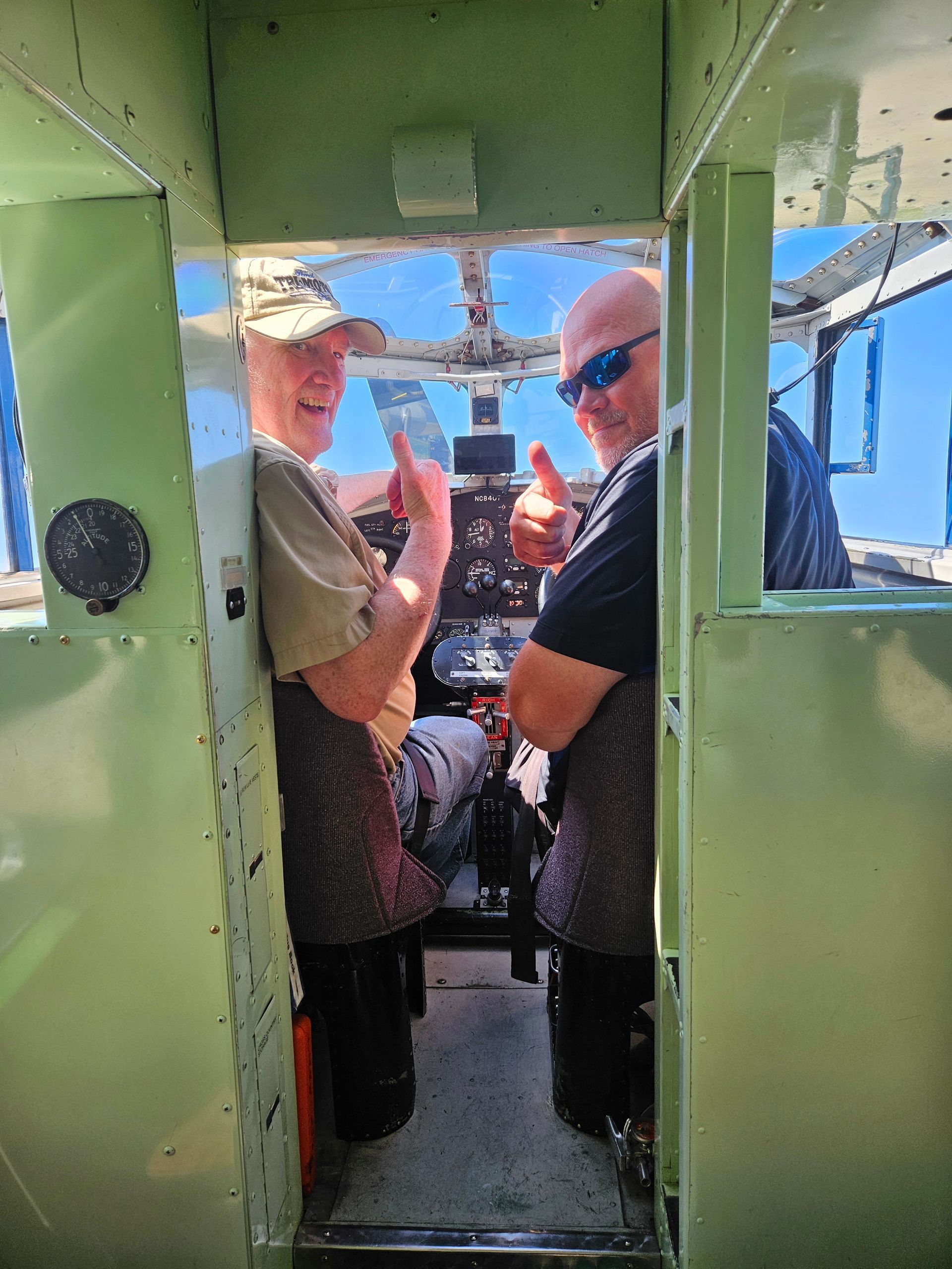 Two men are giving a thumbs up in the cockpit of an airplane
