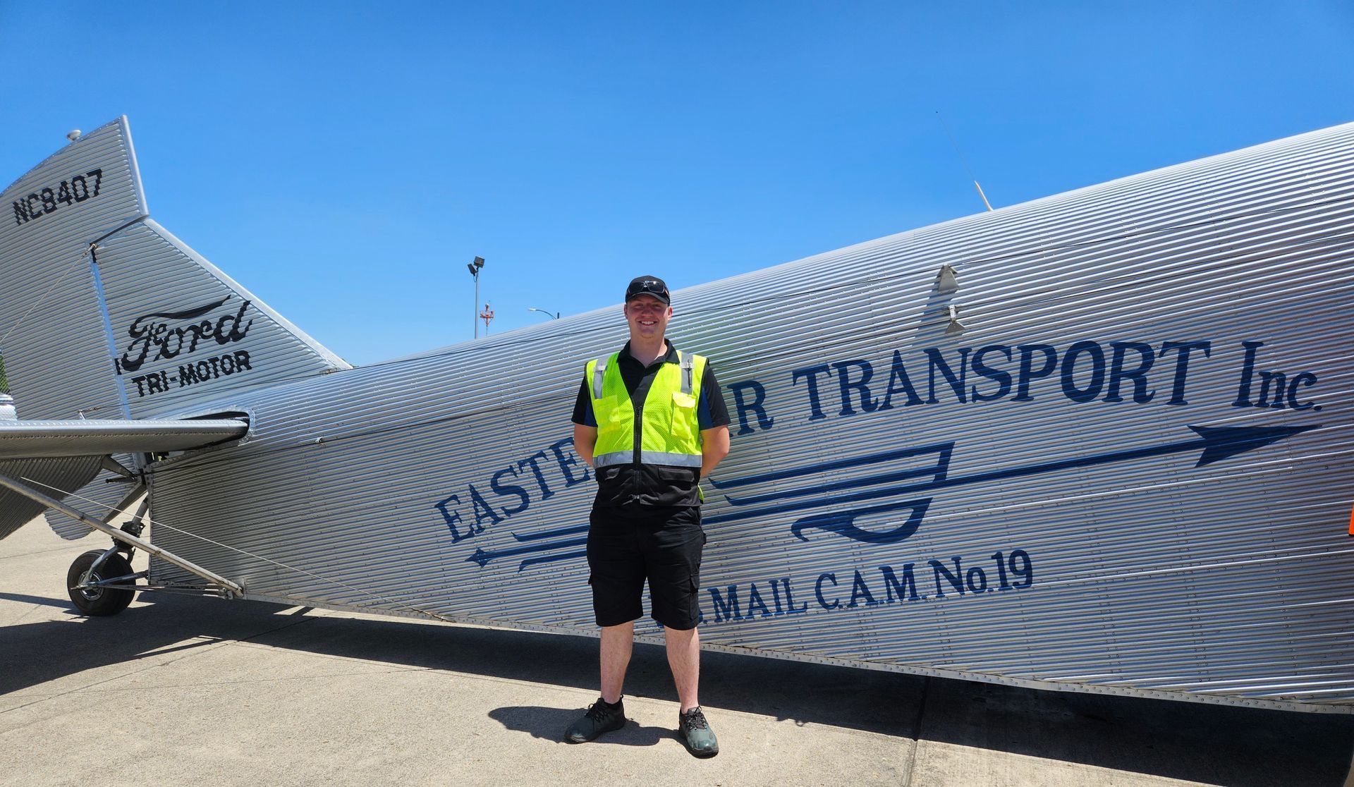 A man in a yellow vest is standing in front of an airplane.