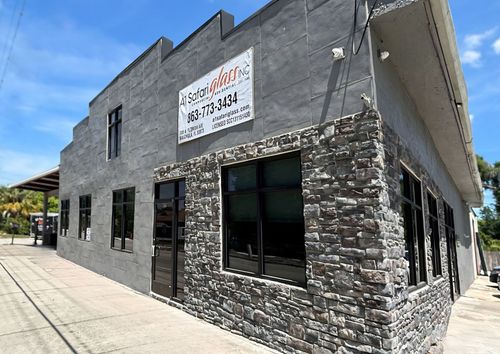 Gray corner building with stone facade, large windows, and a sign above the entrance on a sunny street.