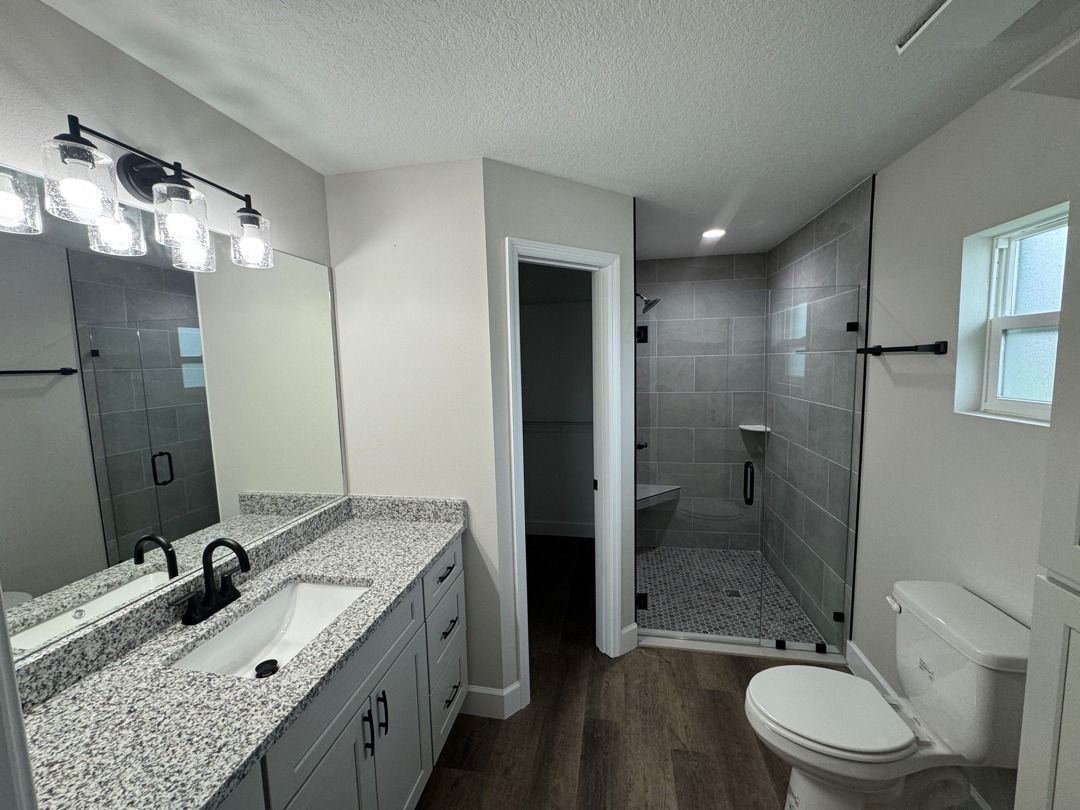 Modern bathroom with double vanity, large mirror, toilet, and gray tiled shower.