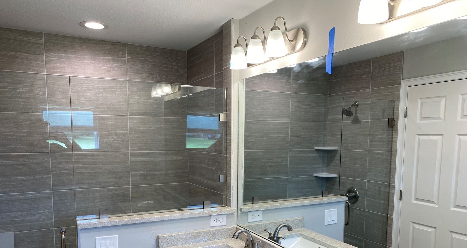 Bathroom with gray tiled shower, glass enclosure, vanity mirror, and white door.