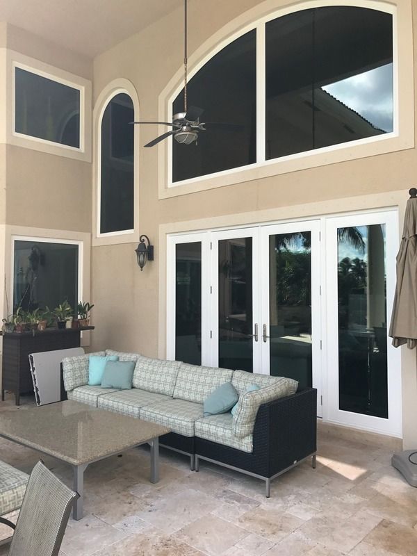 Covered patio with white French doors, arched windows, gray outdoor sofa, and wicker chairs.