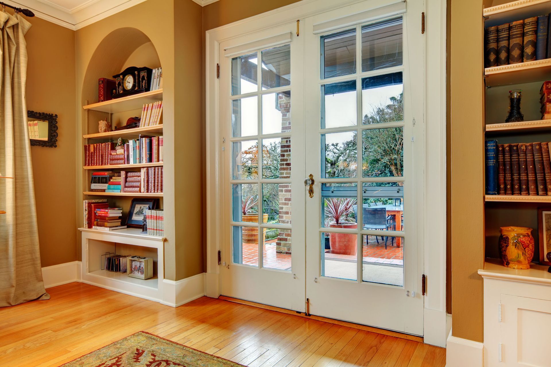 Sunny home library with French doors, built-in bookshelves, and warm wood floors