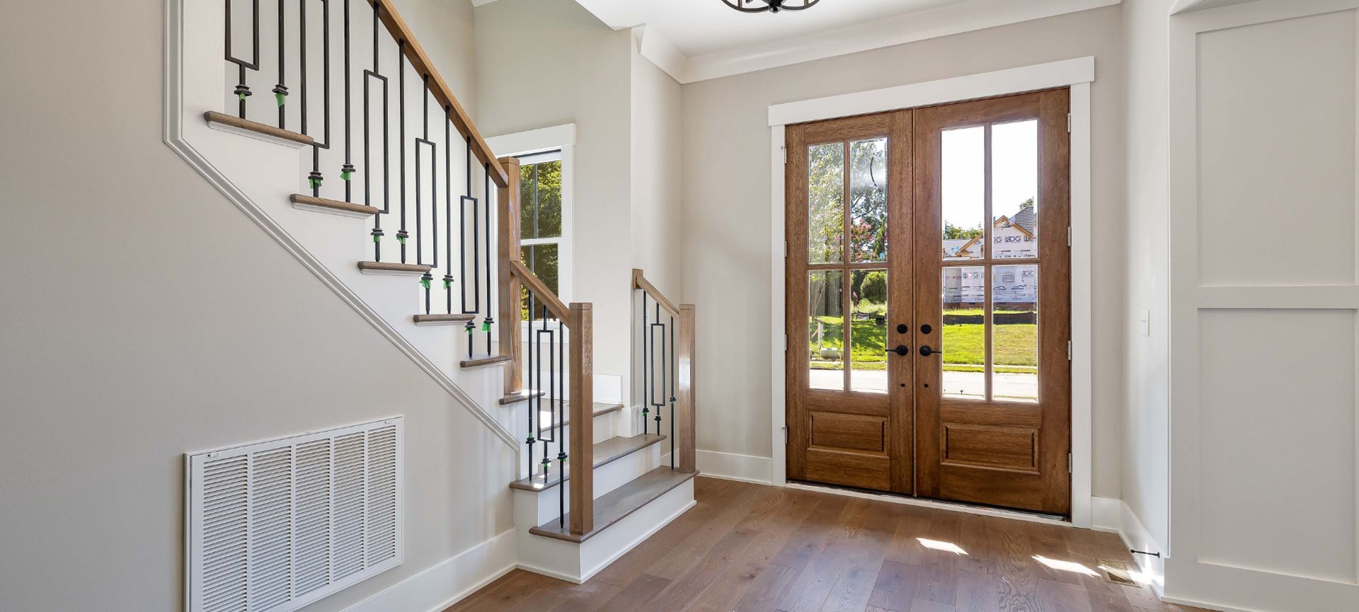 Bright entry hall with wood floors, staircase, and glass double front doors overlooking a yard.