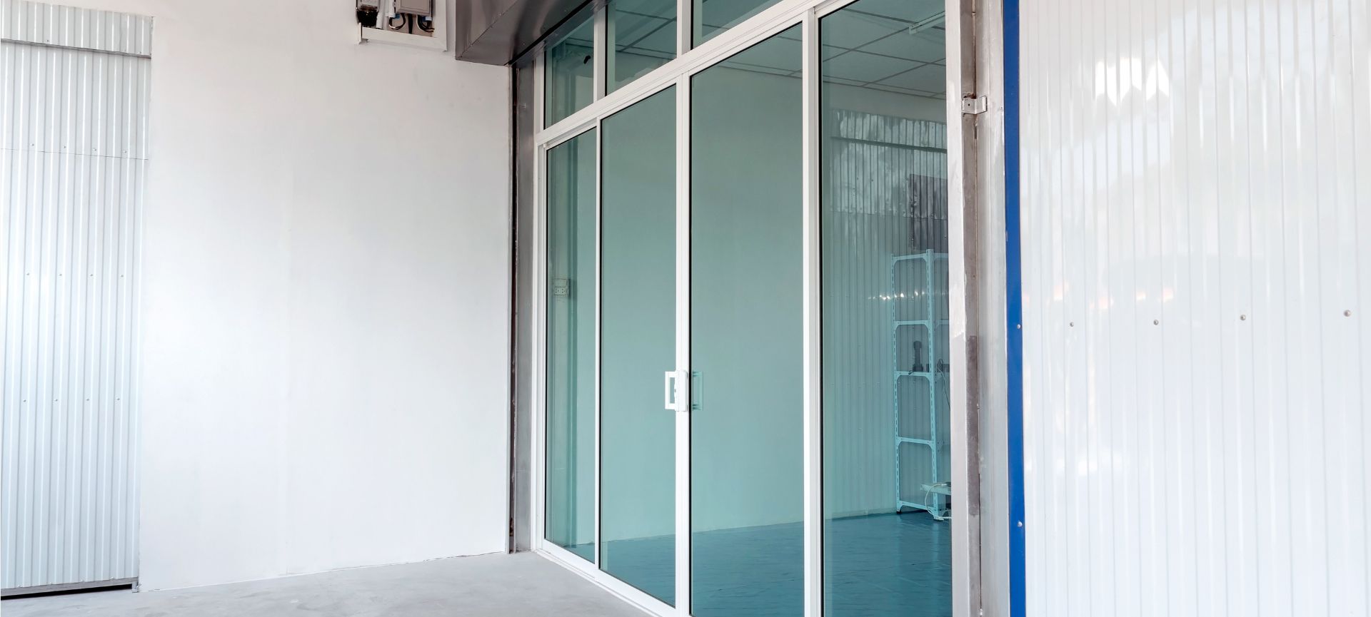 Impact glass sliding doors in a white modern hallway with blue-tinted glass panels.