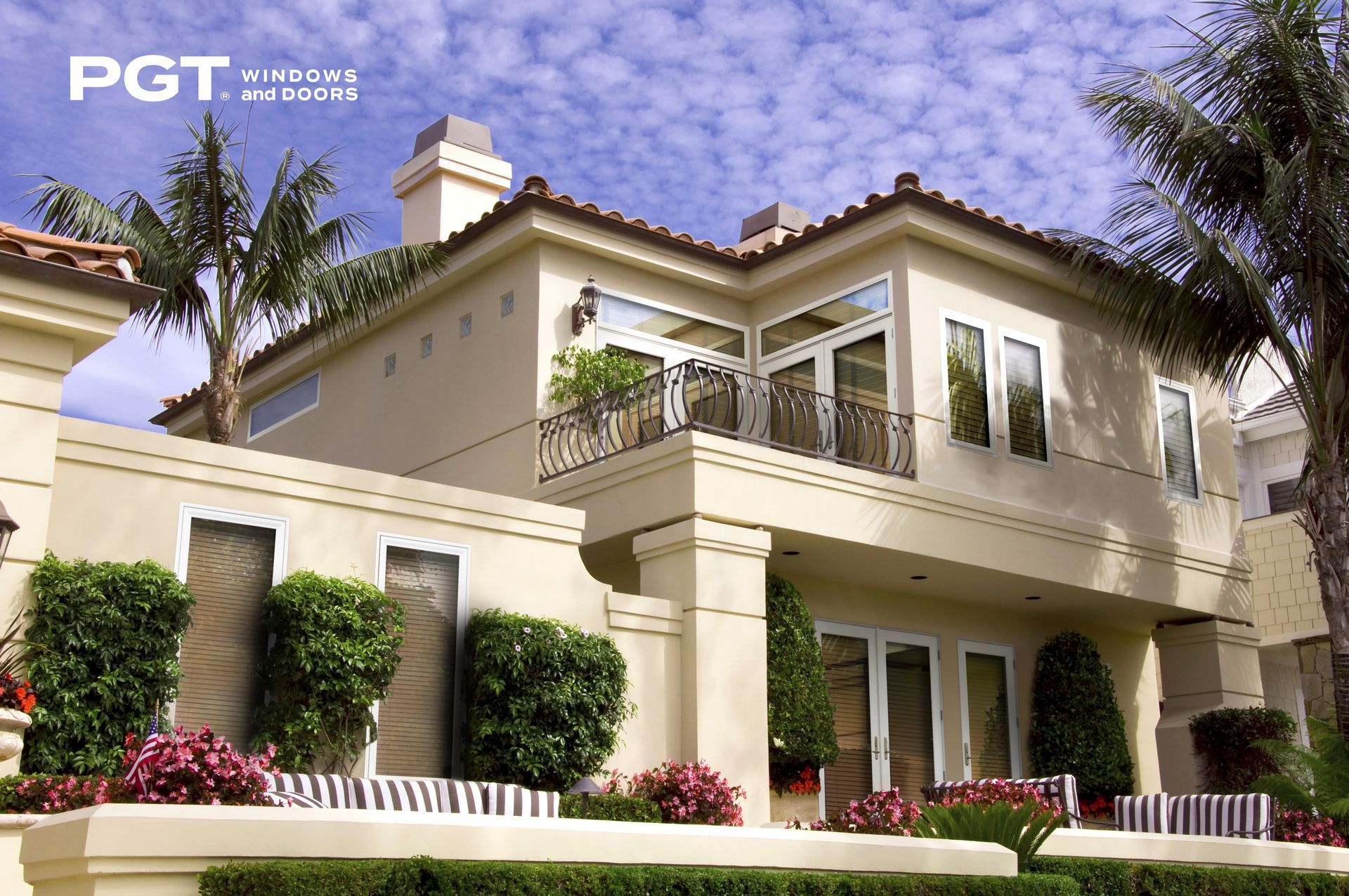 Luxury beige two-story house with balcony, white trim, and landscaped front garden under a blue sky